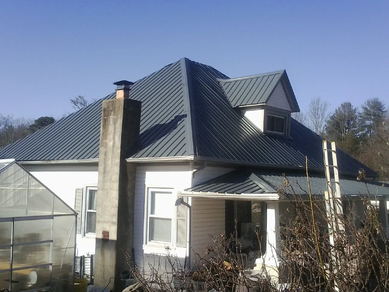 Dark blue standing seam metal roof on a white farmhouse with dormer — Slate & Tile Roof Repair by Roofing Brothers in Udall