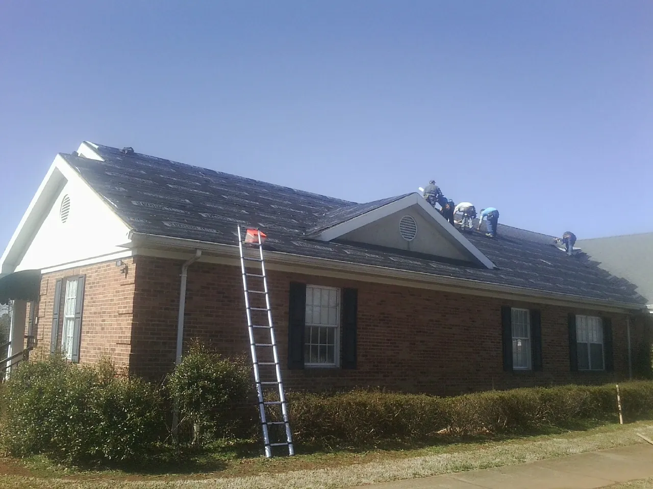 Crew tearing shingles off a brick ranch roof with a ladder set — Emergency Roof Repair work by our crew in Udall