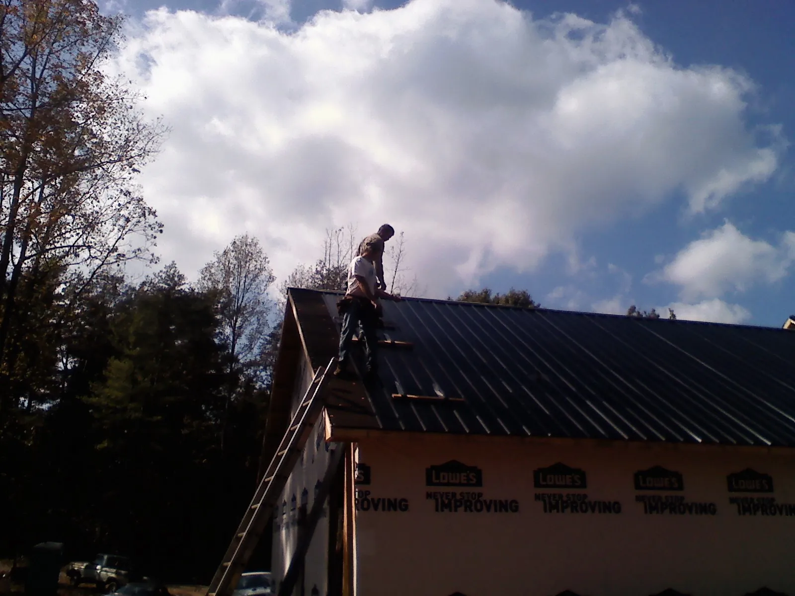 Roofer fastening dark metal panels high against a cloudy sky, from a Roof Inspection job in Udall