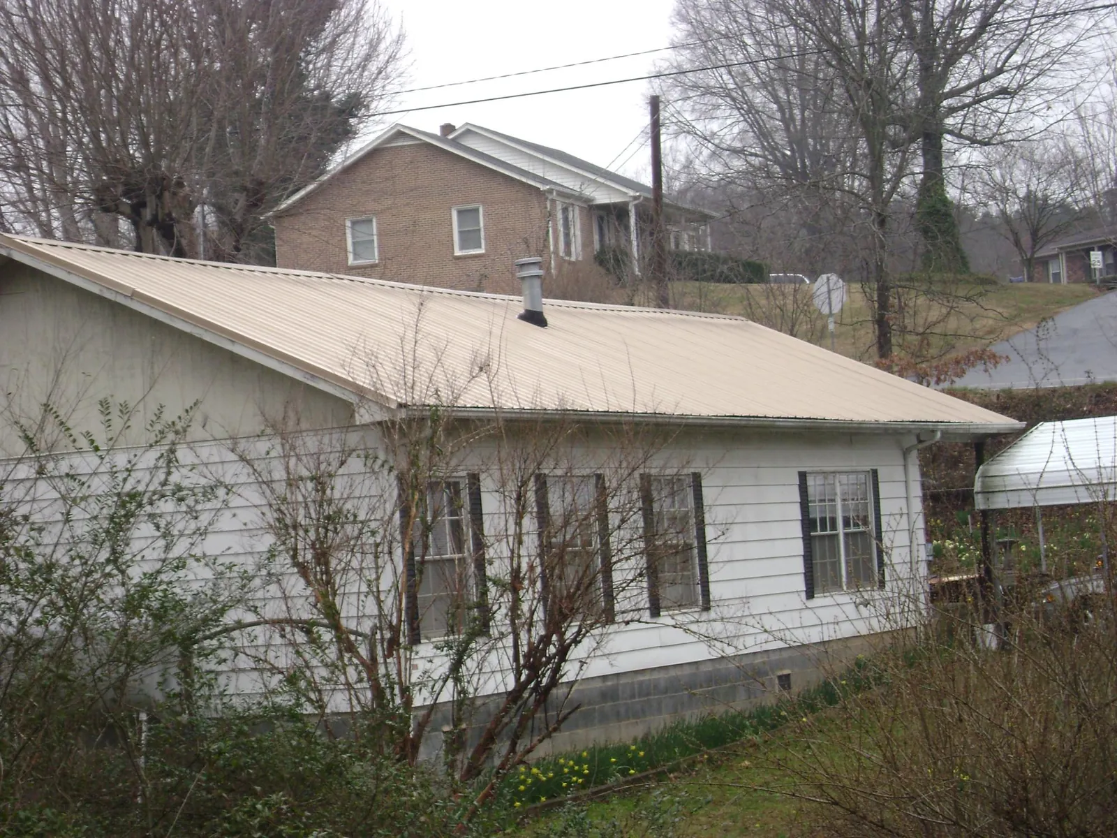 Tan metal roof on a white sided house set into a hillside — Commercial Roofing by Roofing Brothers in Udall
