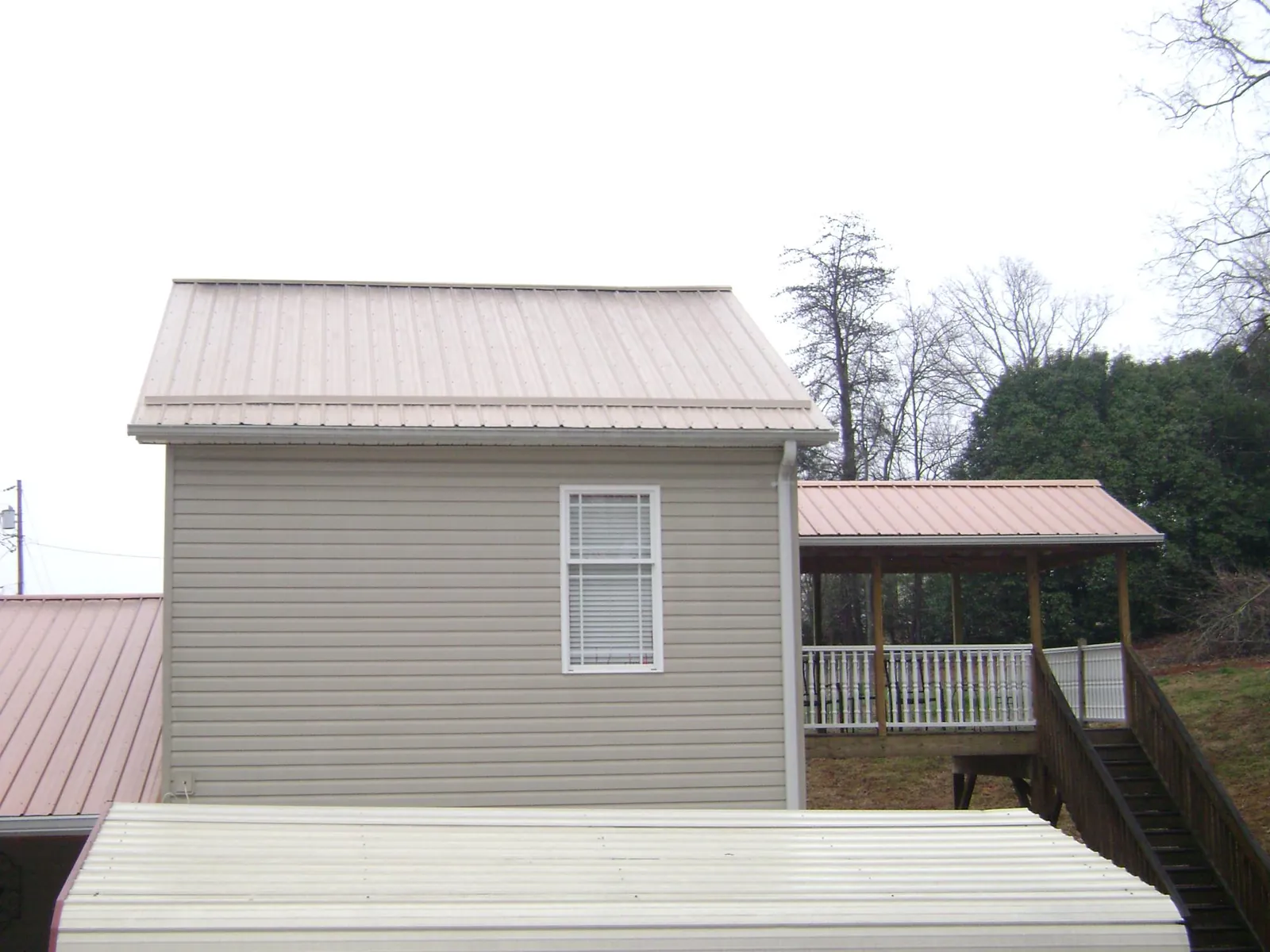 Tan metal roofs on a two story addition and attached porch, from a Roof Replacement job in Udall